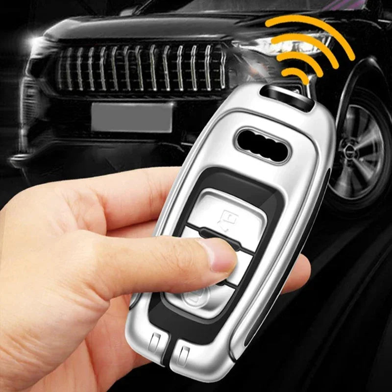 A hand holds a silver key fob cover for an Audi Q5 vehicle with a signal icon visible on the car in the background.