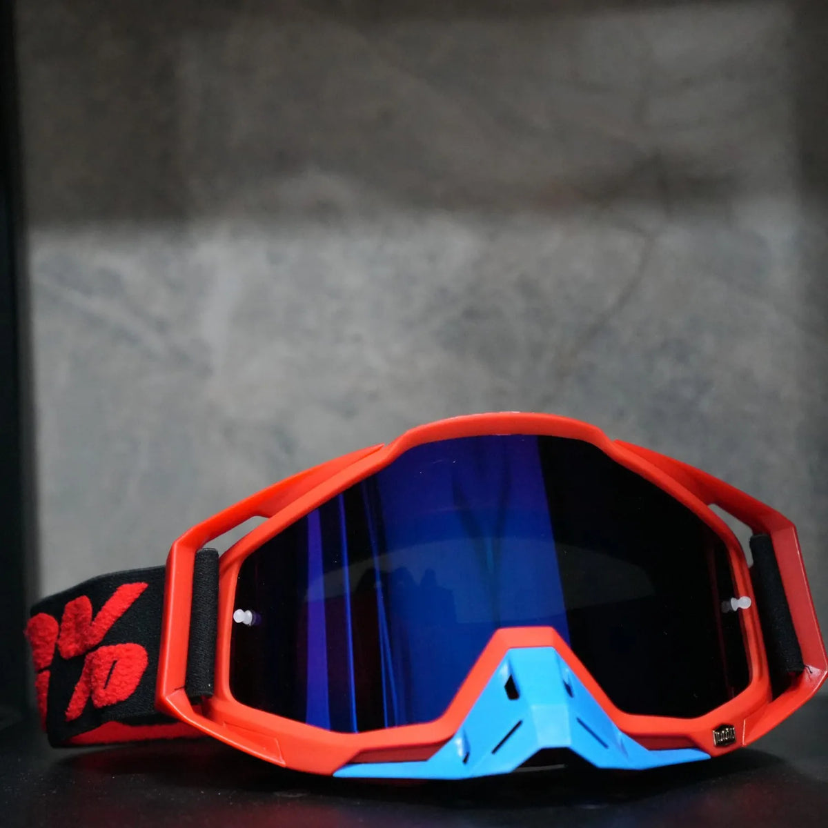 Orange and blue high-performance motocross goggles resting on a dark surface.