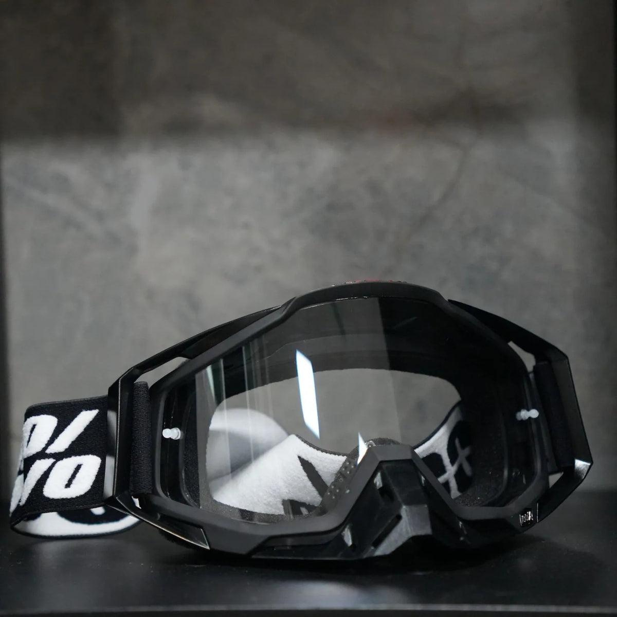 A pair of black high-performance motocross goggles resting on a dark surface.