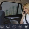 A blonde woman is using a mobile phone while looking through the tinted window of a car.