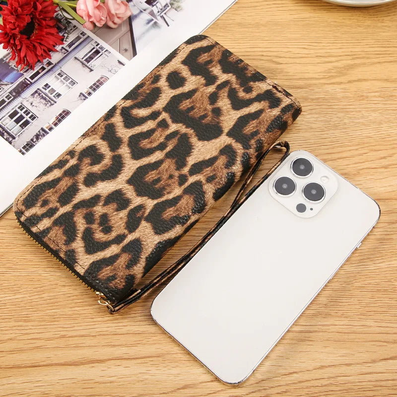 A leopard print long wallet resting on a wooden surface next to a white smartphone.