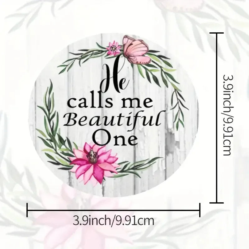 A circular watercolor design featuring pink and green floral wreaths and a butterfly, with the text He calls me Beautiful One