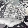A white microfiber cleaning glove is shown resting on a dark surface covered in soapy water and bubbles.