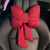 A red bow knot car neck pillow is shown resting on a dark gray car seat.