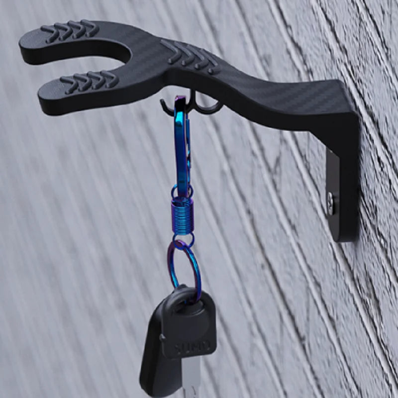 A black wall mount hook with a curved, serrated shape and a blue carabiner attached.