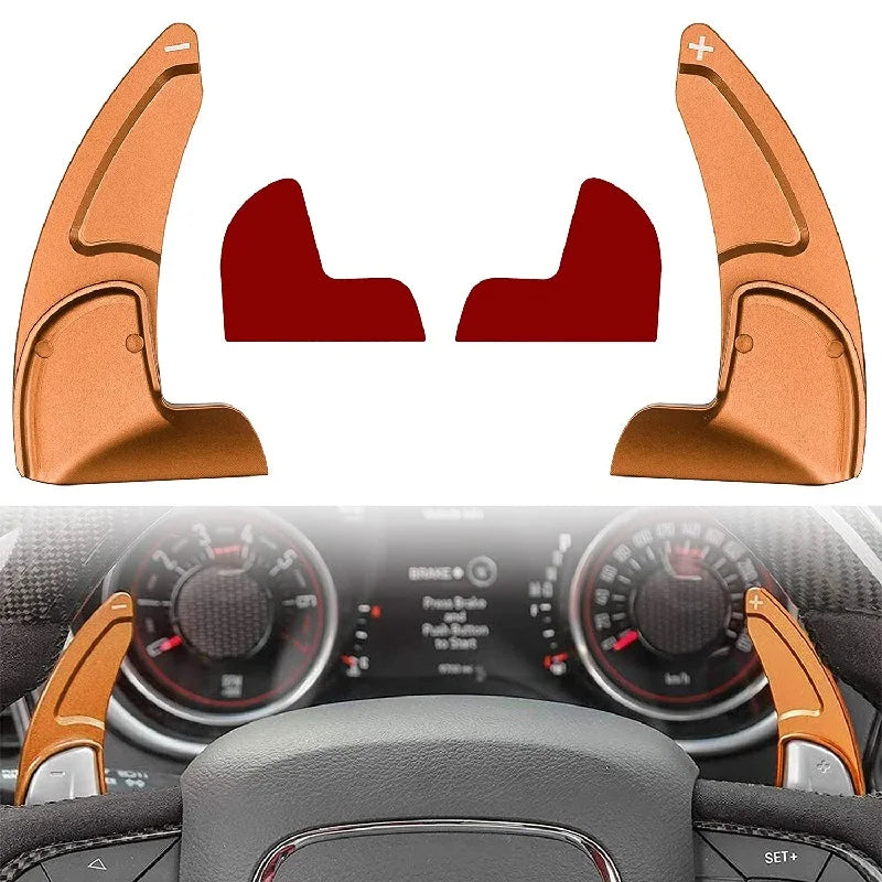 Two orange aluminum steering wheel paddle shifters shown against a dark car interior background.