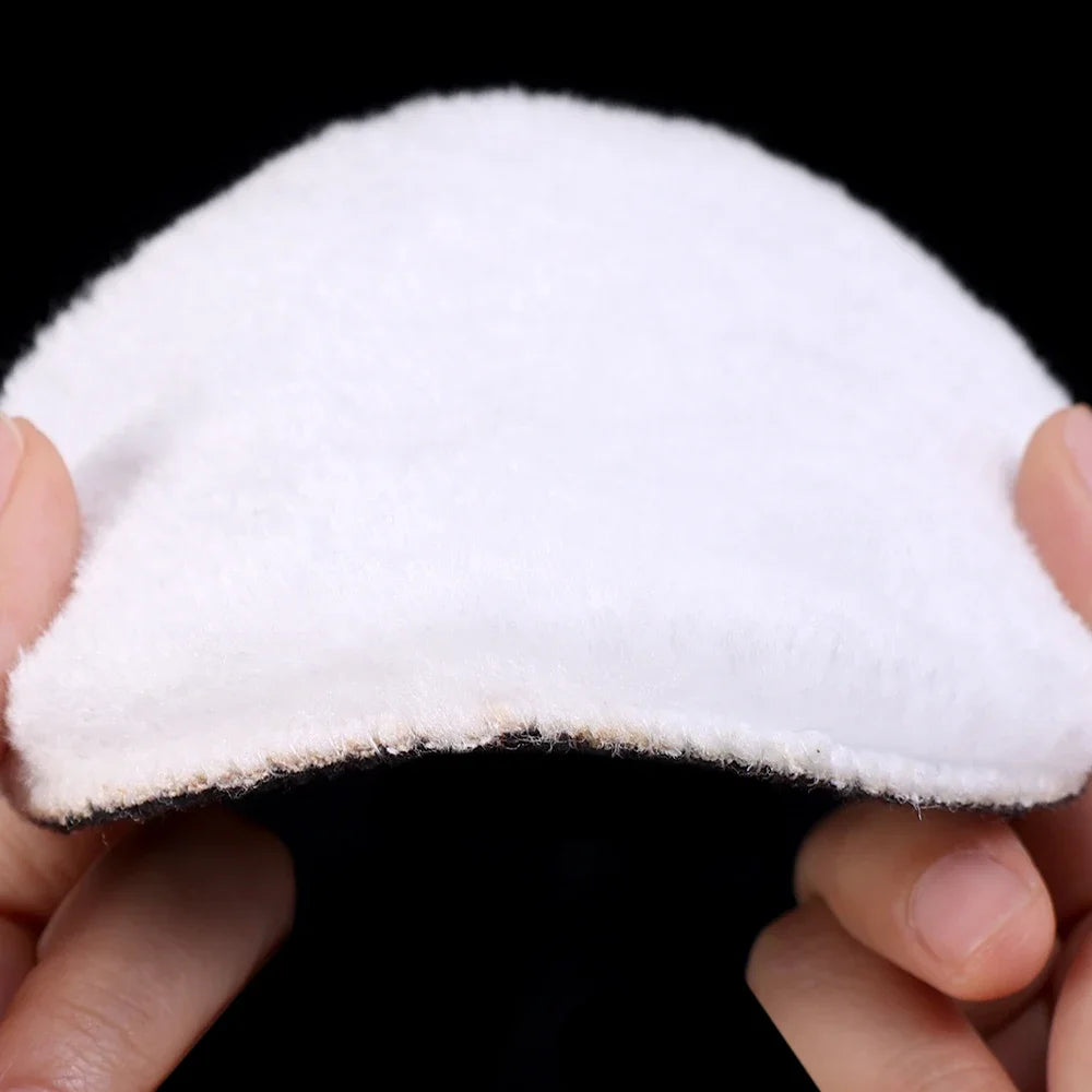 A white polishing disc is held between fingers against a black background.