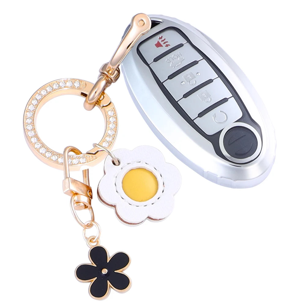 A silver car key fob cover with a gold chain and a white flower charm attached.