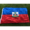 A double-sided polyester flag of Haiti featuring the national colors and coat of arms displayed on a green lawn.