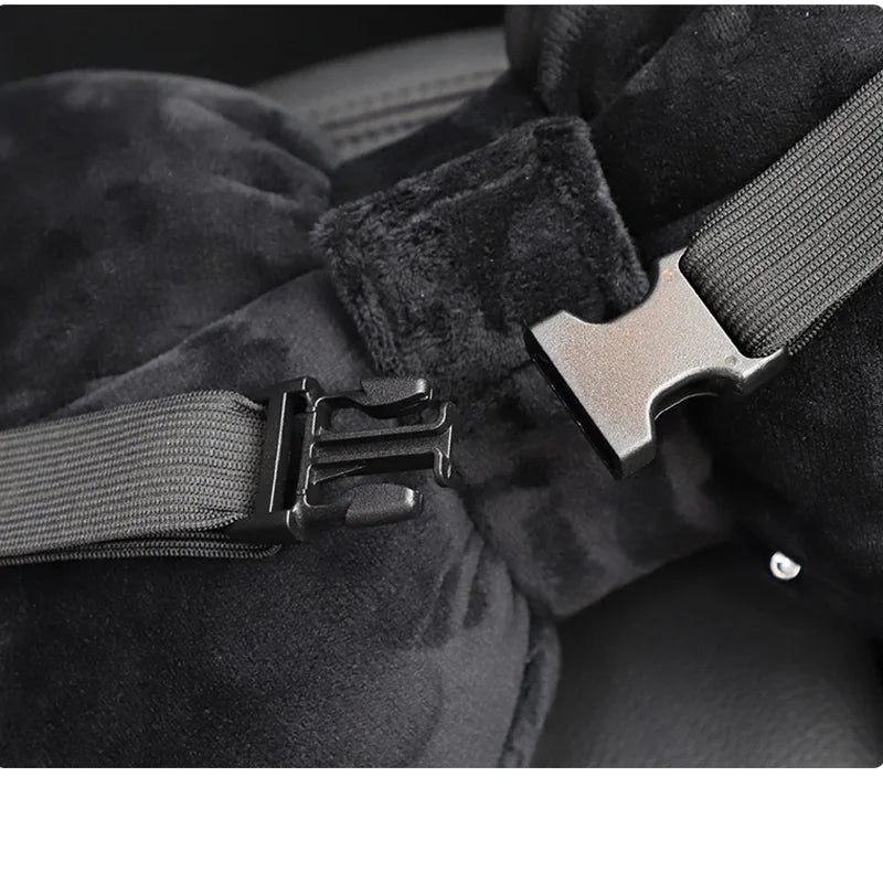 A close-up of a black velvet car neck pillow set with a dark leather strap and buckle.