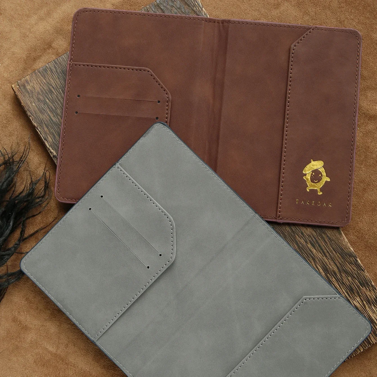 A brown leather passport holder and a gray leather cardholder are displayed on a textured brown surface.