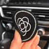 A hand holds a black silicone car cup coaster with a white floral design and clear rhinestones.