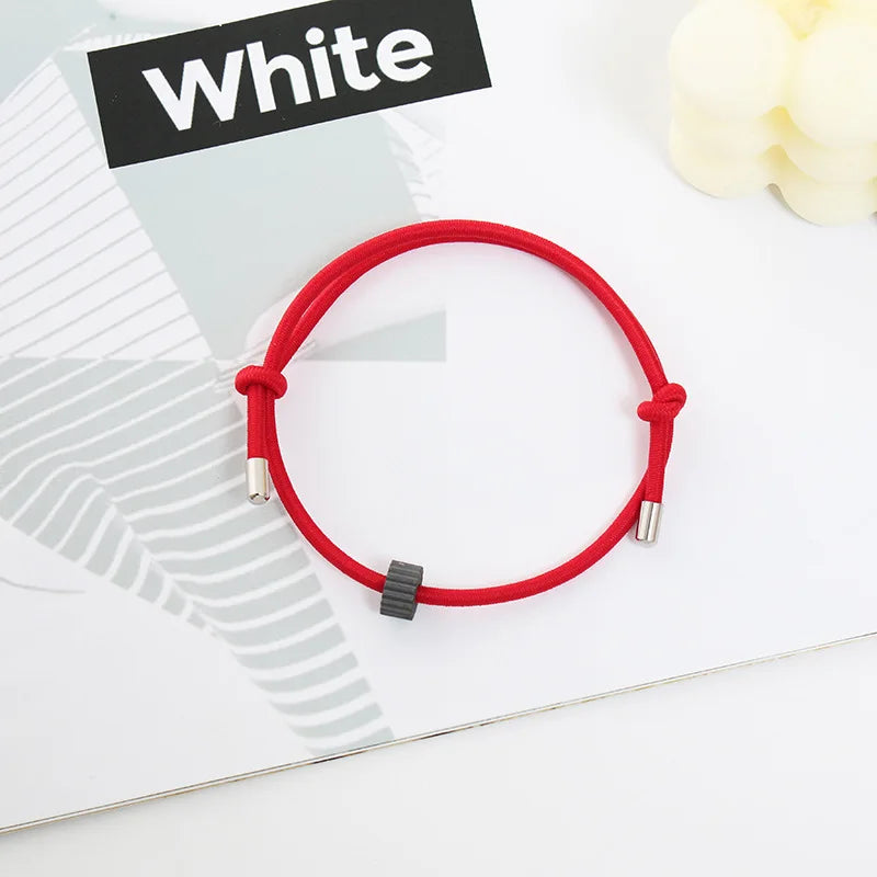 A red heart-shaped fitness tracker bracelet is displayed on a white background next to a black sign reading White.
