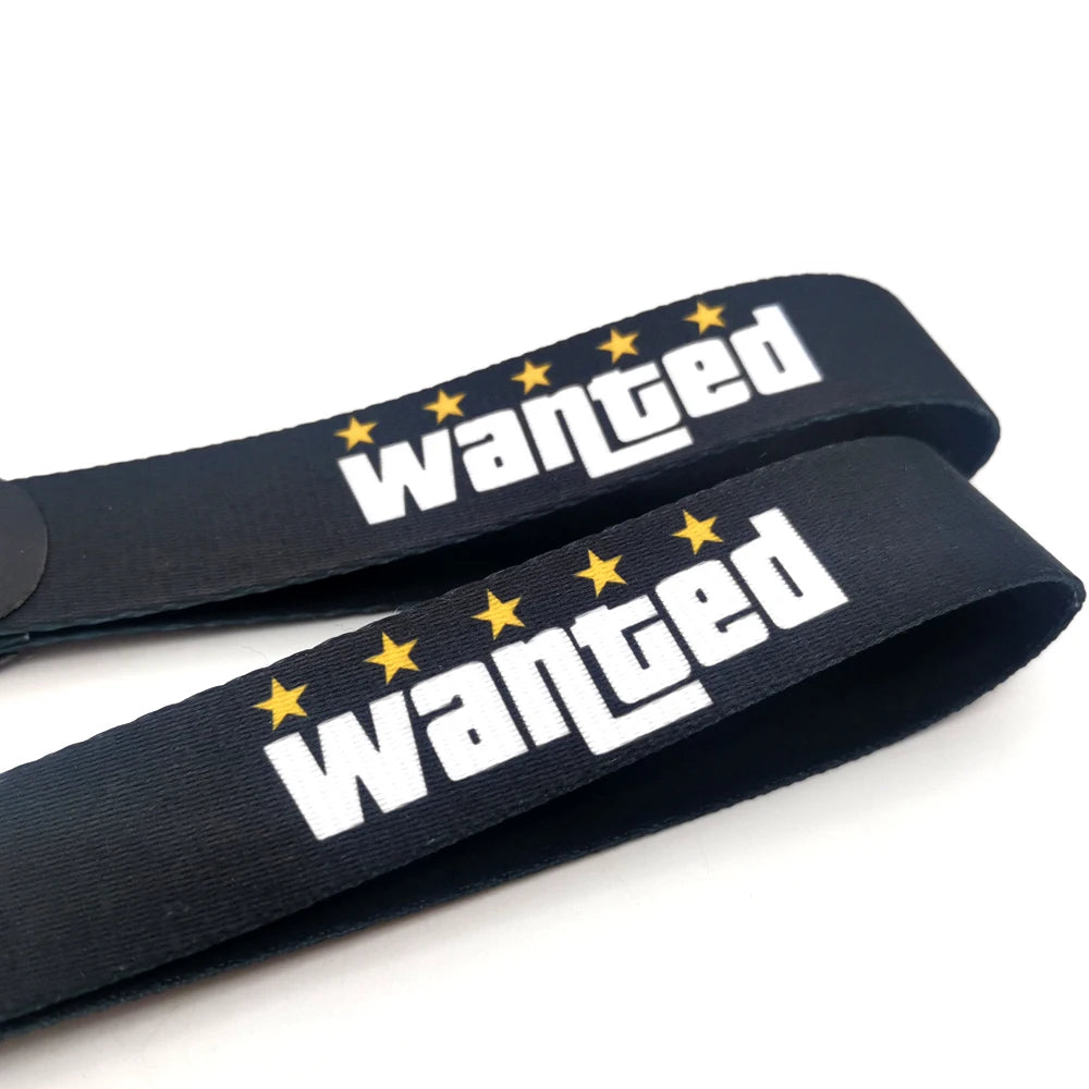 Porte-clés en nylon noir avec texte brodé 'wanted' en blanc et étoiles jaunes.