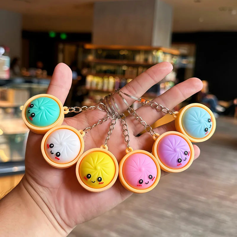 A hand holds several colorful silicone keychains shaped like cute bao buns in various pastel colors.