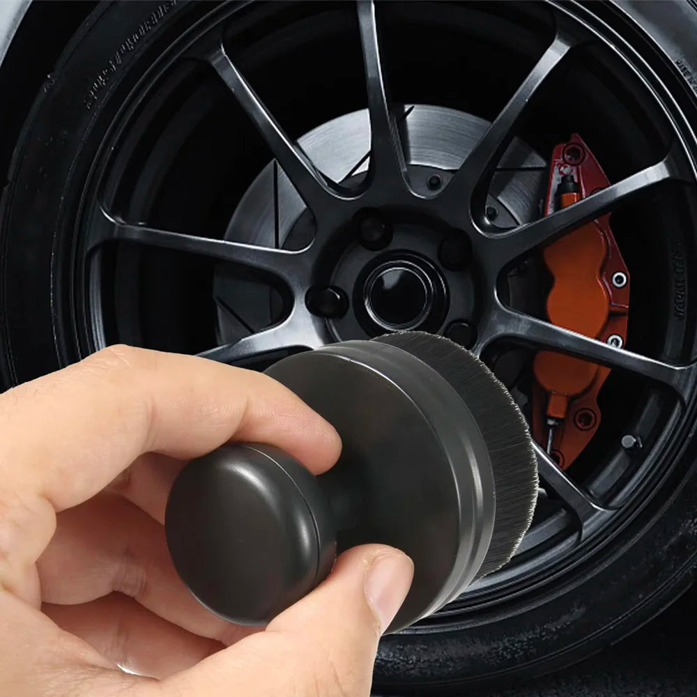 Une main tient un kit de brosse de detailing noir placé dans un jante de voiture.