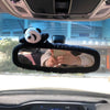 A panda plush toy is placed on a black rearview mirror cover inside a car.