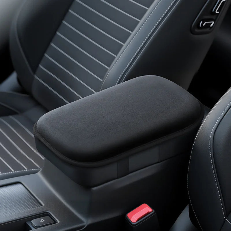 Nahaufnahme einer schwarzen Autoarmlehnenpolster-Boosterpad mit Nähten und einem roten Knopf.