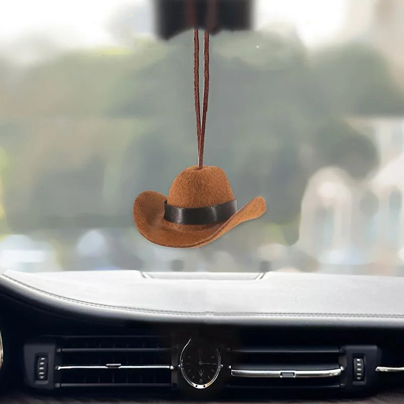 A brown fabric cowboy hat ornament is hanging from a string above a black car interior.