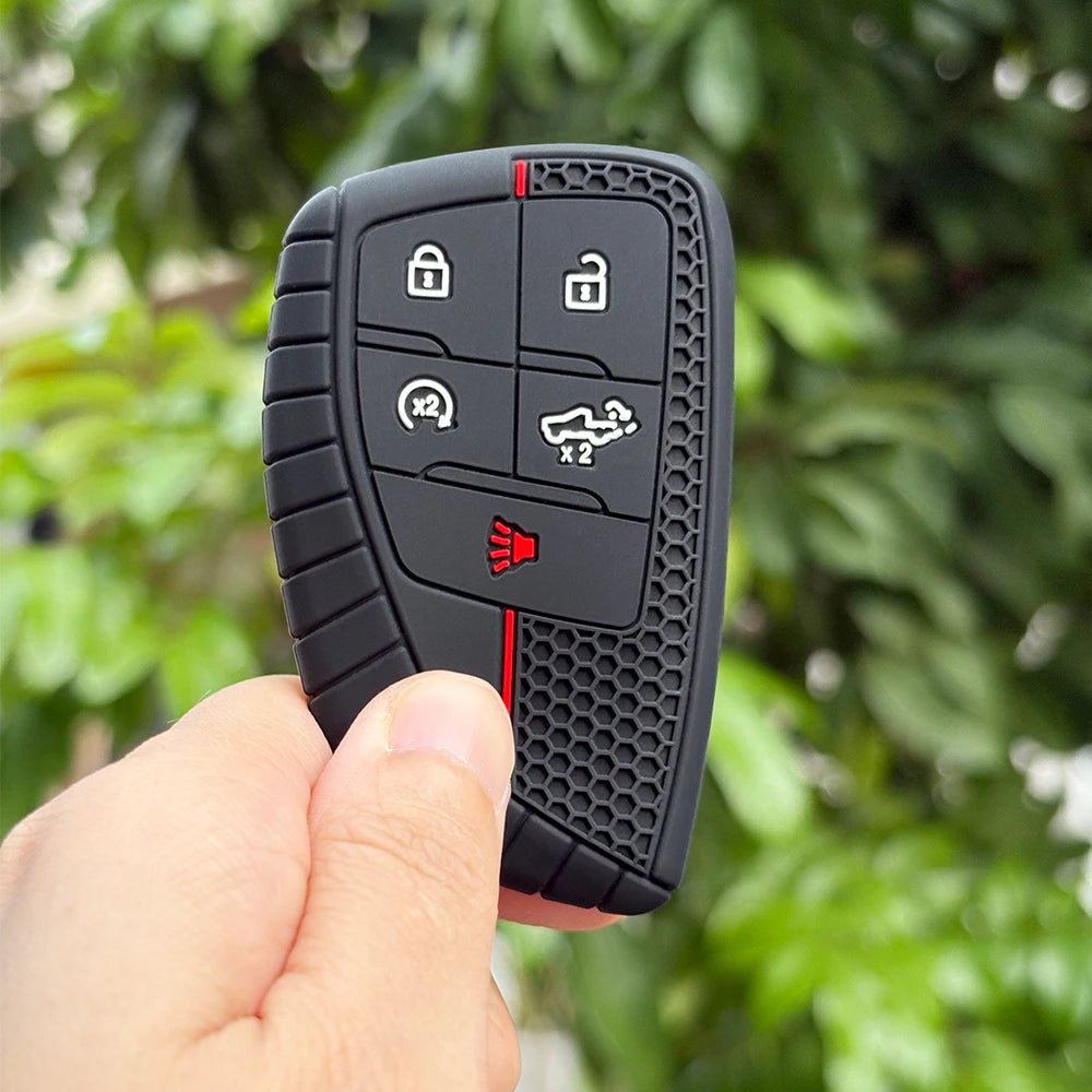 A hand holds a black universal key fob cover with various buttons and a red indicator light.