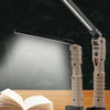 A portable working lamp with multiple light sources illuminating an open book on a wooden surface.