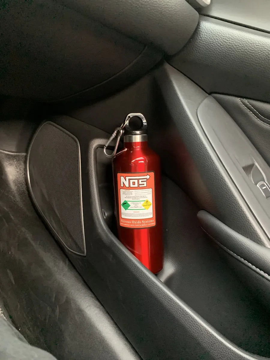 A red insulated stainless steel travel kettle hanging in a car interior door panel.