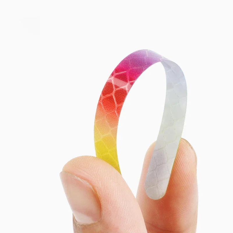 A hand holds a curved, multi-color reflective safety sticker with a gradient of pink, orange, yellow, and white.