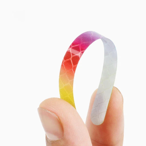 A hand holds a curved, multi-color reflective safety sticker with a gradient of pink, orange, yellow, and white.