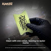 A hand wearing a black glove holds a yellow silicone tool for cleaning car film, with water droplets visible in the backgroun