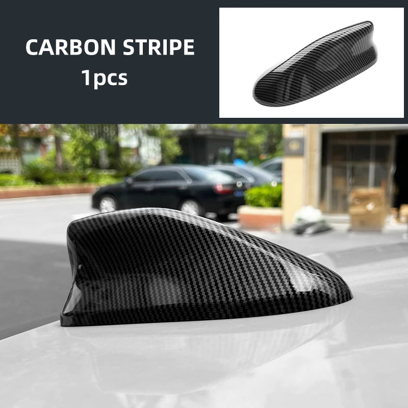 Black carbon stripe shark fin roof antenna cover placed on a white car surface.