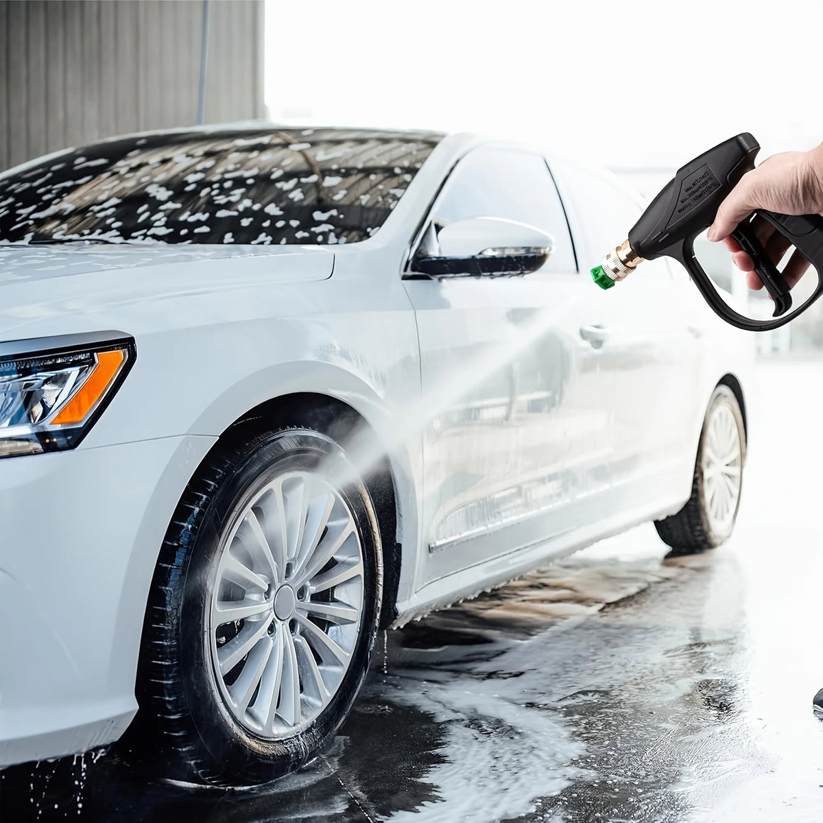 A hand sprays water onto a white car's exterior with a professional high-pressure cleaning gun.