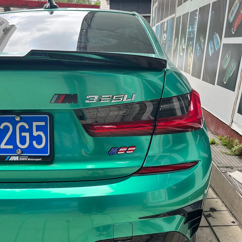 A close-up view of a green BMW sports car with black trim and red taillights, featuring tri-color 3D car grill decals.