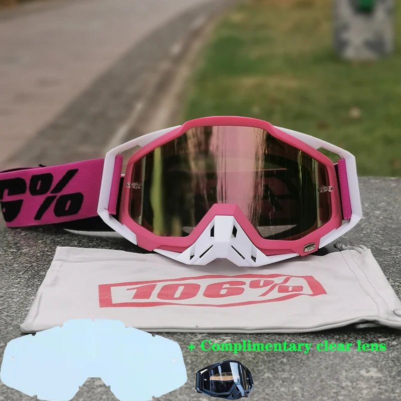 Pink and white durable motocross goggles resting on a gray surface with a cloth and a clear lens.