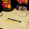 A small glass jar of transfer gel next to yellow and brown samples labeled black and orange.