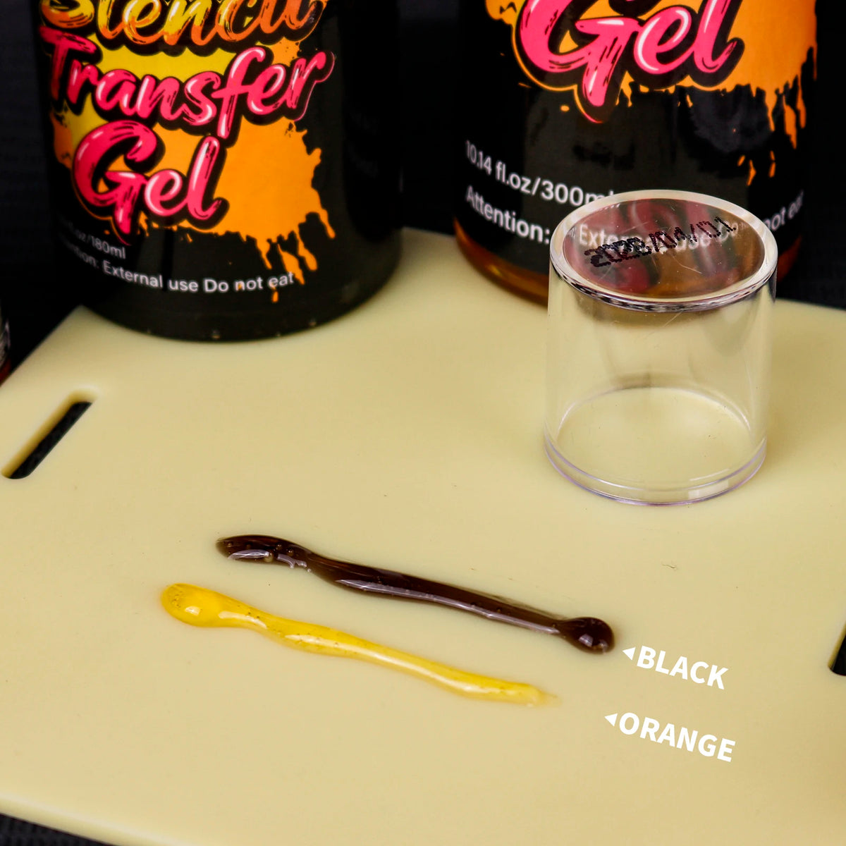 A small glass jar of transfer gel next to yellow and brown samples labeled black and orange.