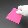 A hand wearing a white glove is using an anti-scratch PPF squeegee on a bright pink window tint film.
