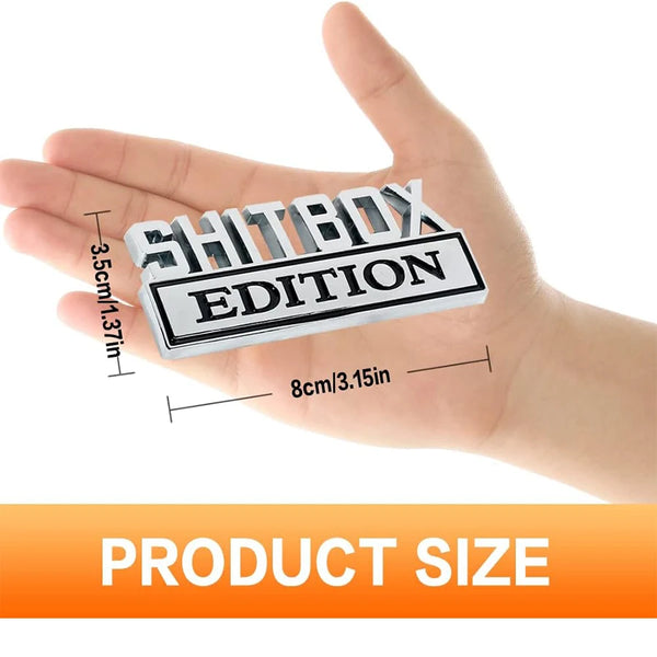 Una mano sostiene un conjunto de calcomanías con el logo Shitbox Edition en blanco y negro, mostrando su tamaño en relación c