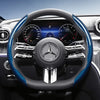 Close-up view of a black steering wheel with blue carbon fiber texture accents and a Mercedes-Benz instrument cluster.