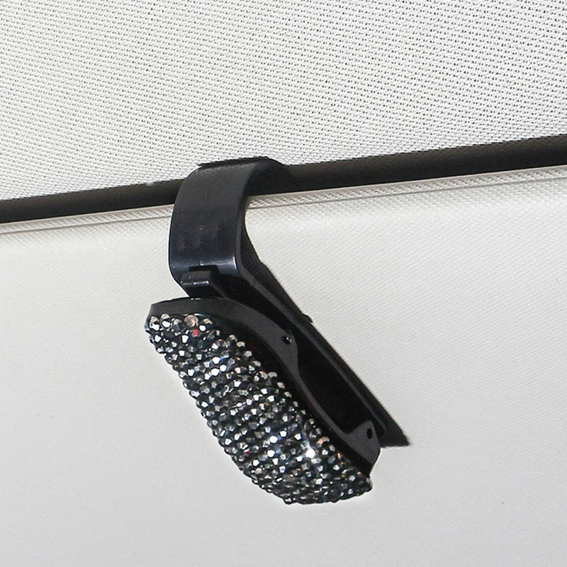 Schwarzer Halter für Sonnenbrillen mit Kristallakzent, montiert auf weißer Oberfläche.