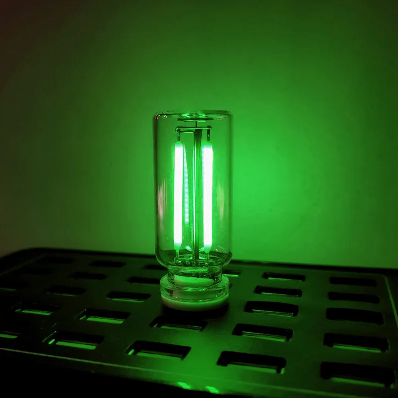 A clear glass LED night light with a bright white glow is placed on a dark metal grid.