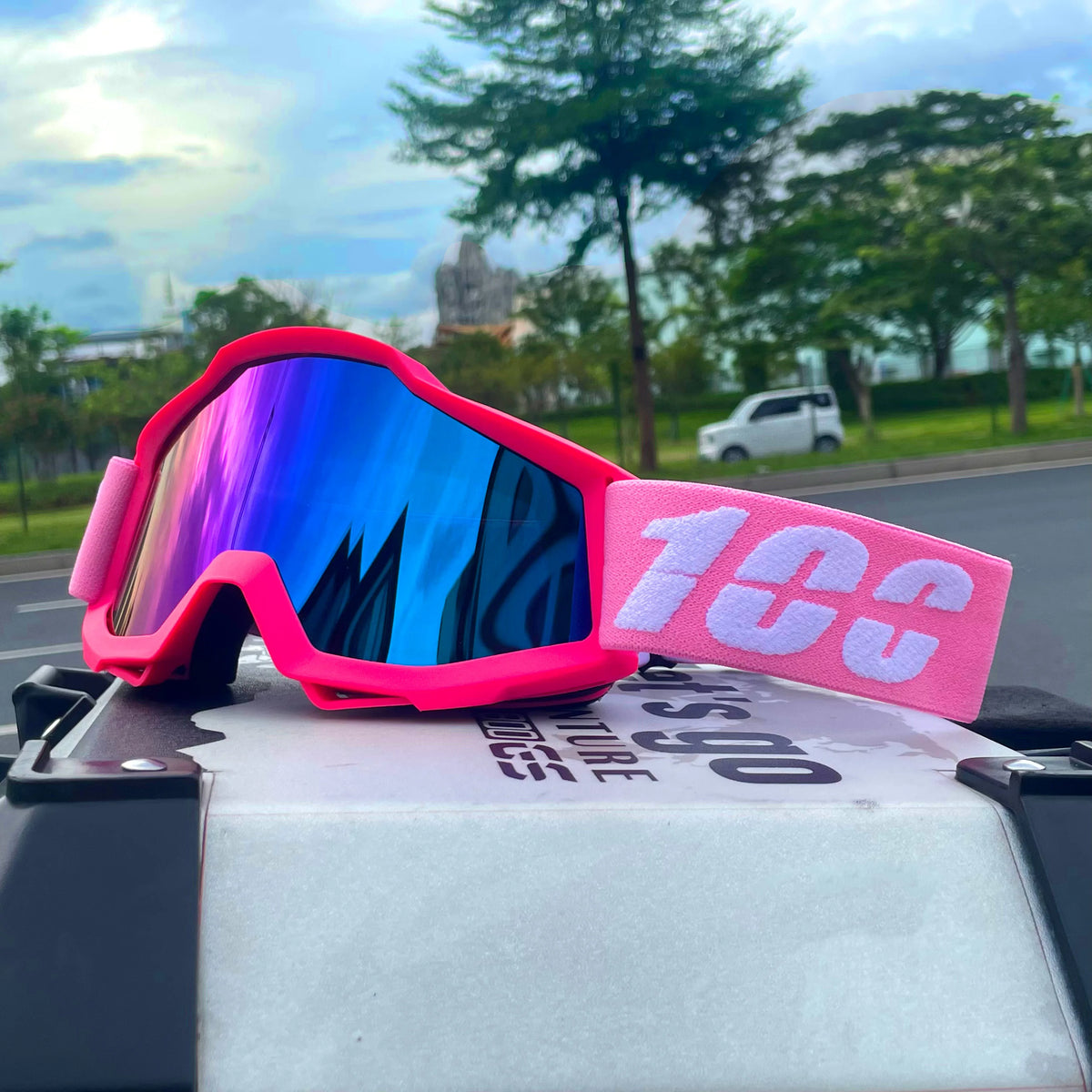 Pink off-road motorcycle goggles with iridescent blue lenses resting on a white box.