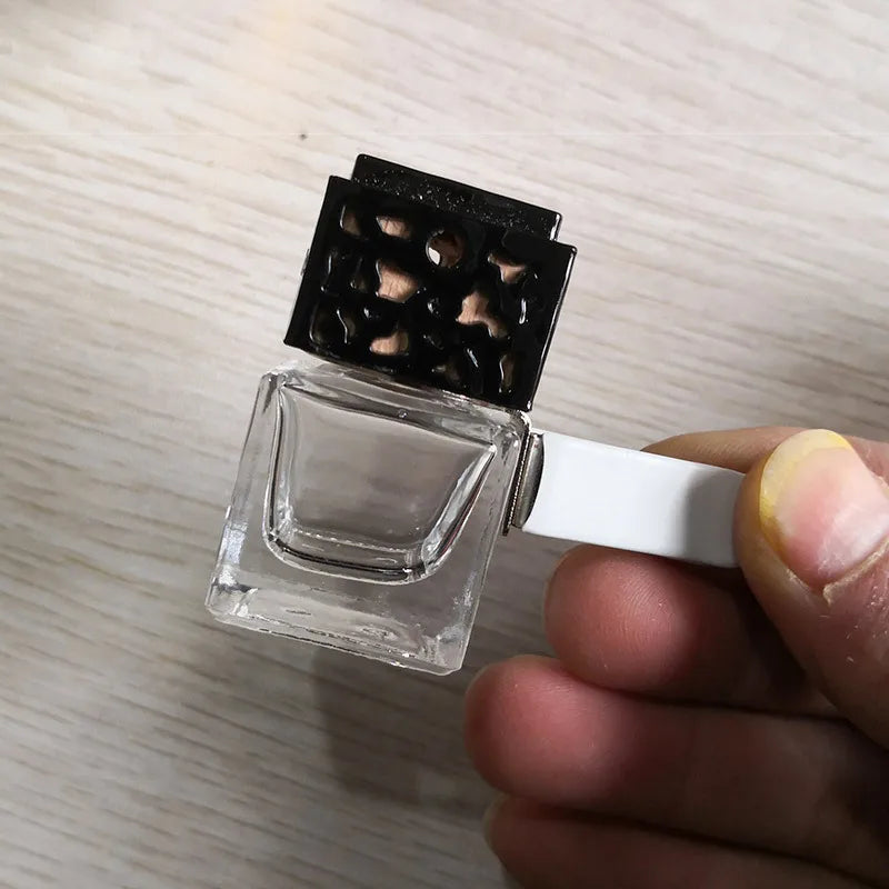 A clear glass car air freshener bottle with a black mesh top is held in a hand.