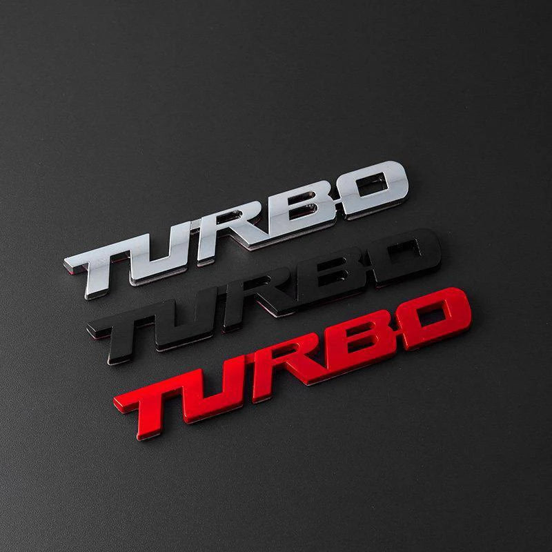 Three metallic badges spelling TURBO in silver, black, and red, displayed on a dark surface.