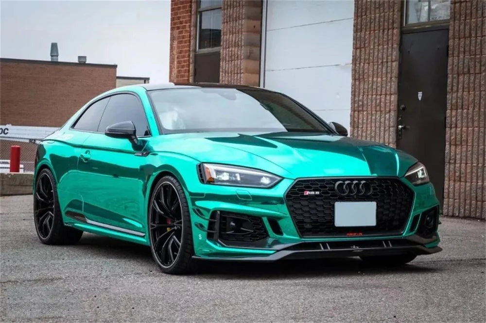 A bright teal Audi sports car with a black wrap parked in front of a brick building.