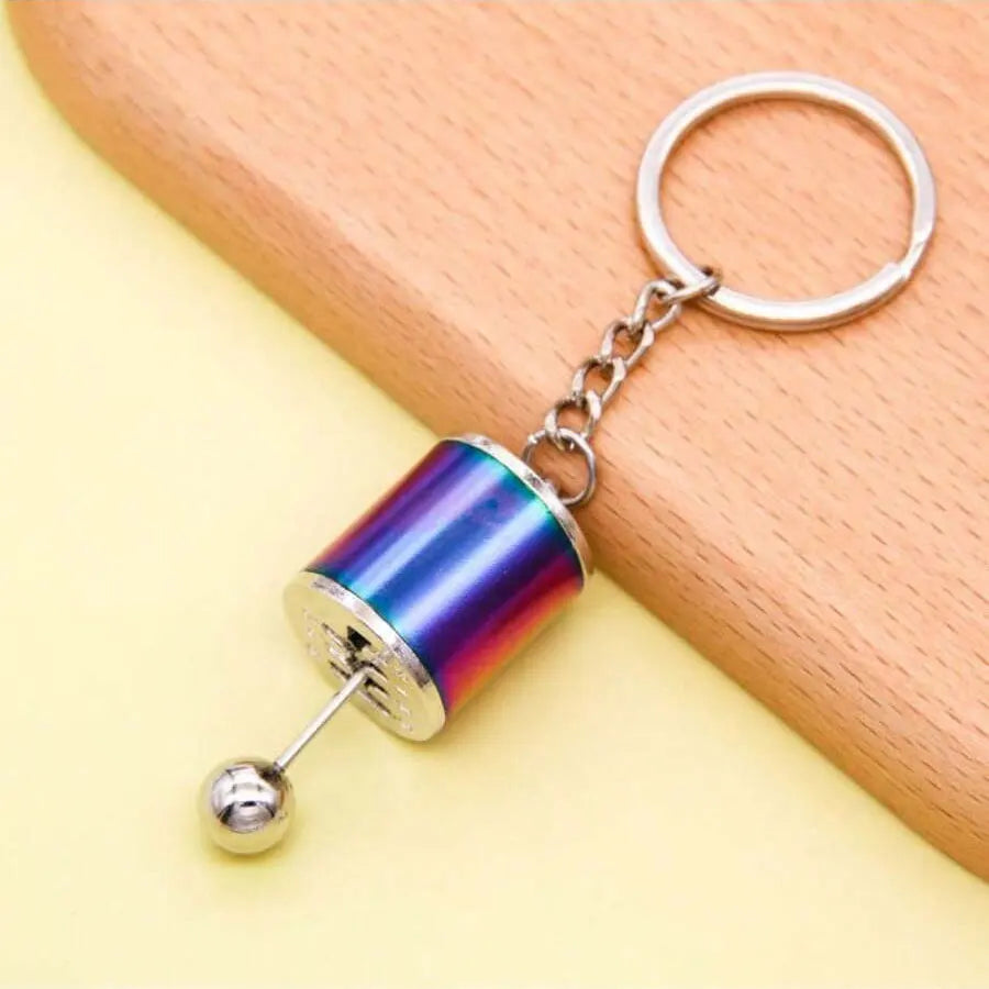 A silver keychain with a colorful, iridescent cylindrical charm attached to a split ring.