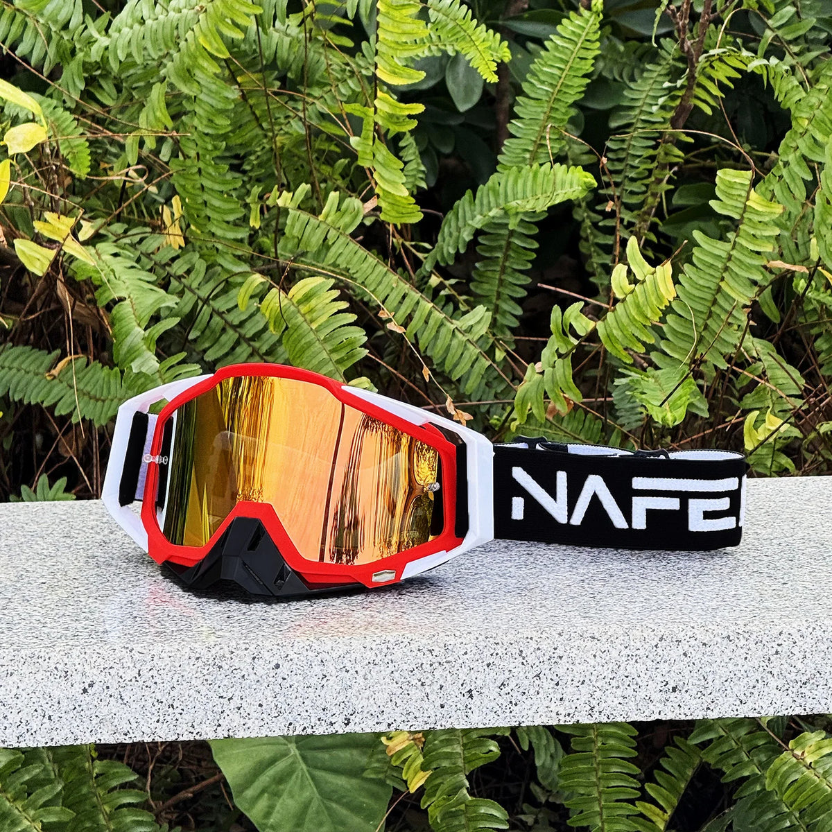 Une paire de lunettes de sport orange et noires posée sur une surface claire parmi le feuillage vert.