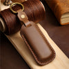 A brown leather car key fob cover attached to a coiled brown leather cord on a wooden surface.