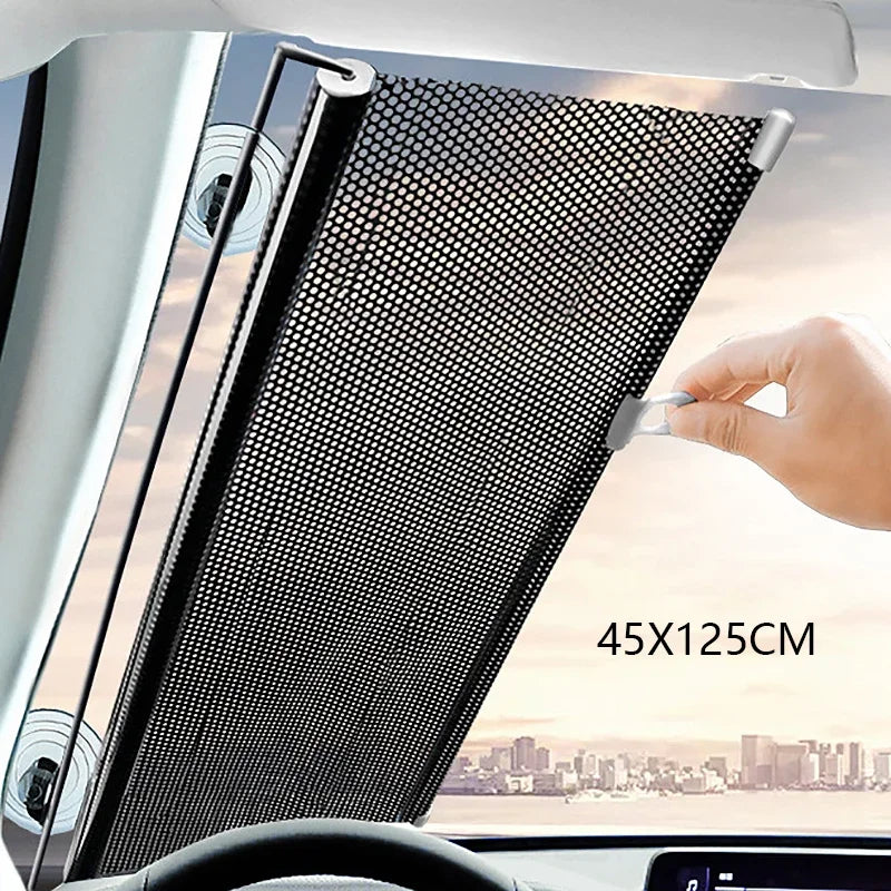 A hand is adjusting a black mesh retractable car windshield sun shade in a vehicle interior.