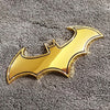 Glänzendes goldfarbenes Batsymbol-Aufkleberabzeichen auf einer dunkelgrauen strukturierten Oberfläche.