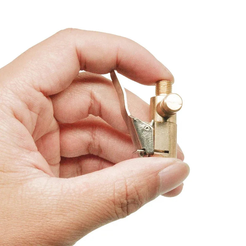 A hand holds a small brass portable inflatable tire pump with a threaded nozzle.